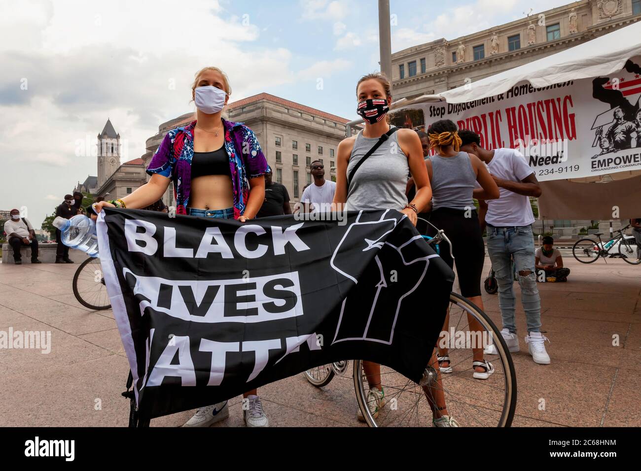 Two protesters hold large Black Lives Matter flag at Black Homes Matter rally at Freedom Plaza, Trump Hotel in distance, Washington, DC, United States Stock Photo