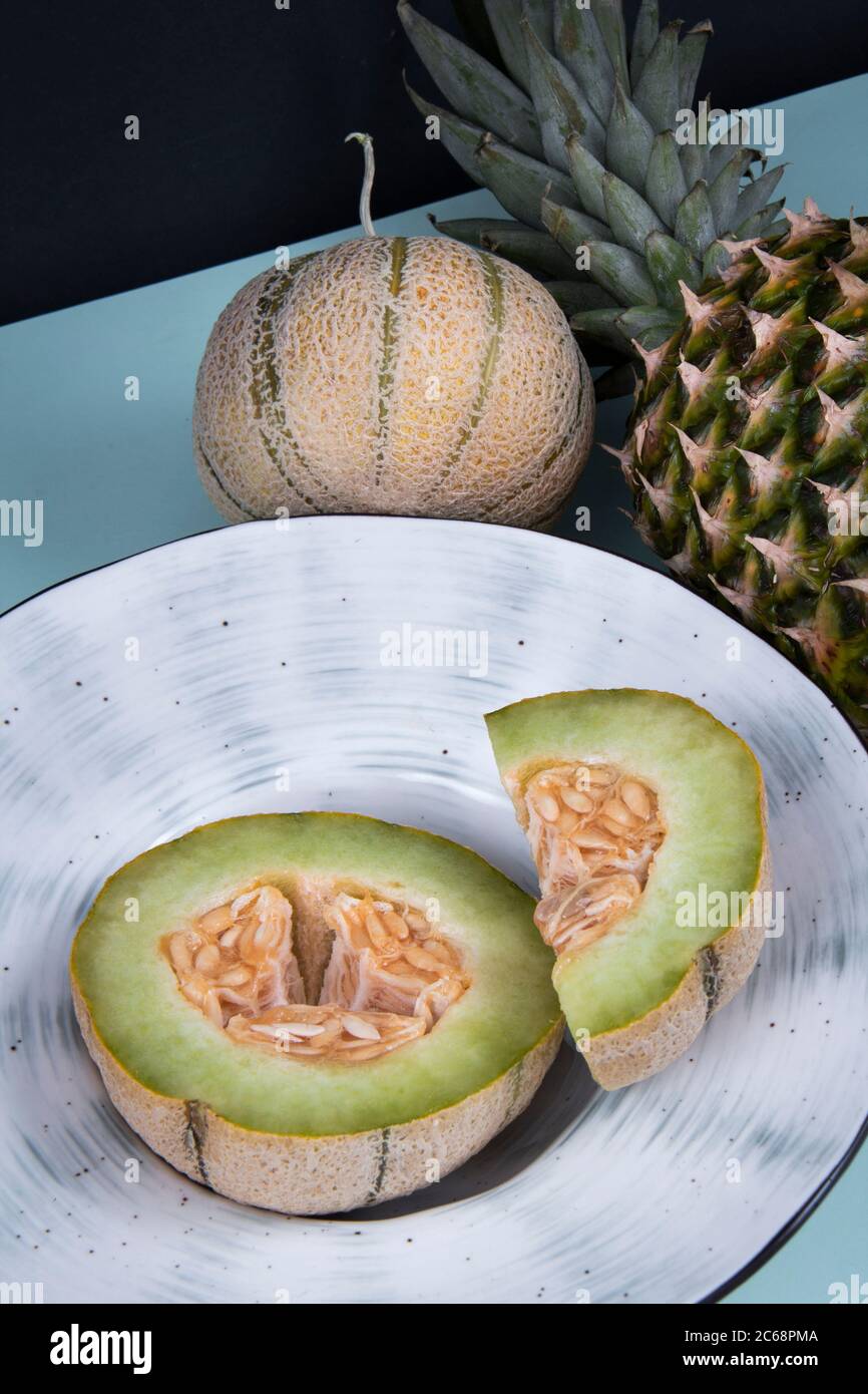 Slices cut of a honeydew melon in a dish near a full melon and a pineapple. Stock Photo