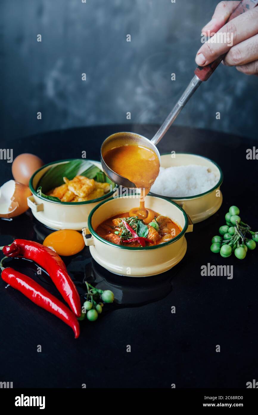 ladle pour Red curry paste serving in tiffin box with raw ingredients
