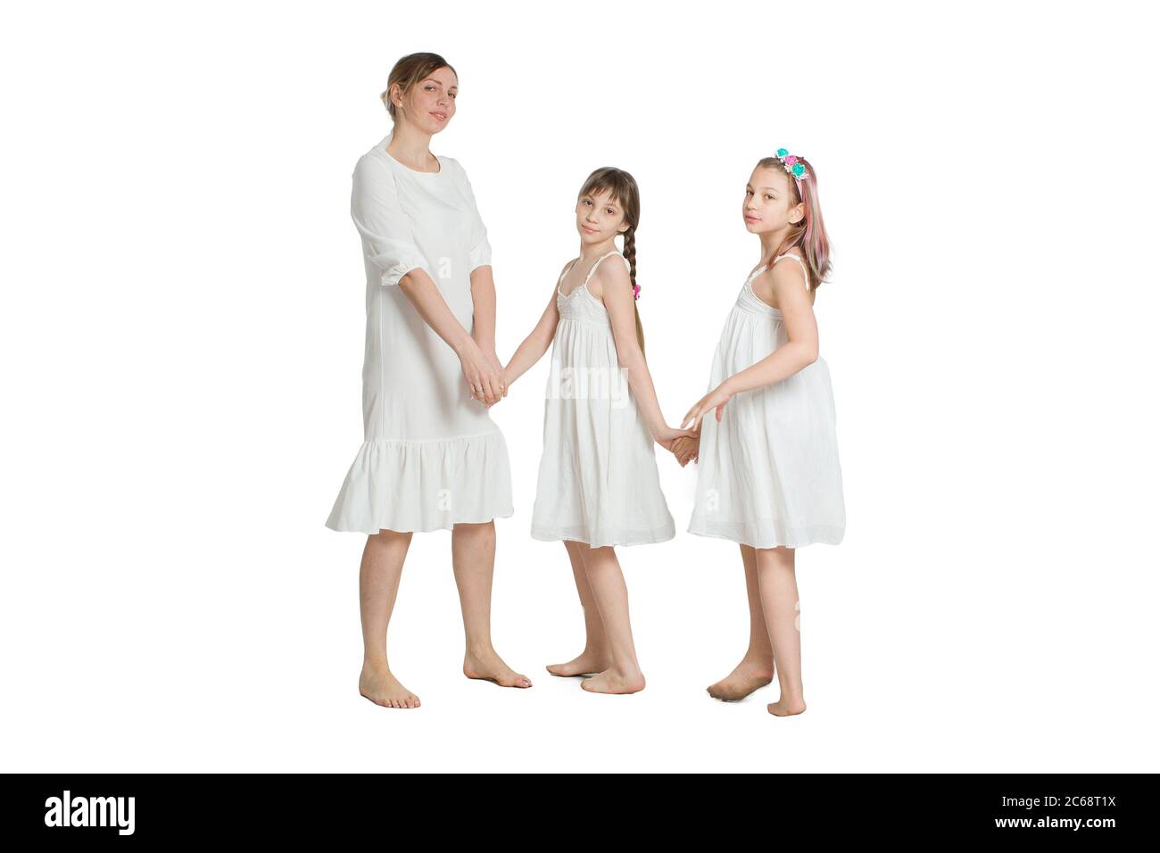 Family mother and two daughters in similar long white dresses. Isolated on white. Stock Photo