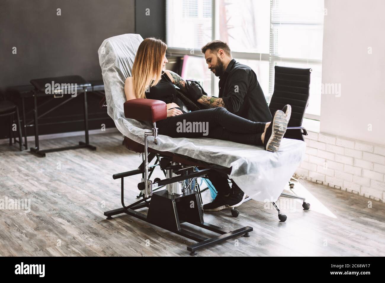 Professional tattooer carefully doing tattoo on girl hand using tattoo machine in modern studio Stock Photo