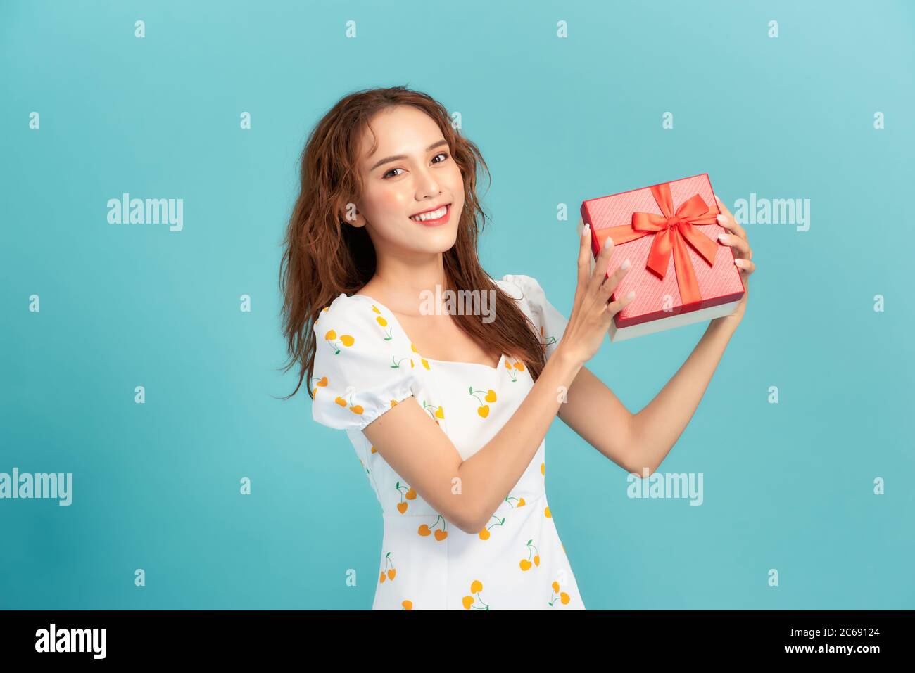 Happy smiling girl in dress holding present box and  over blue background Stock Photo