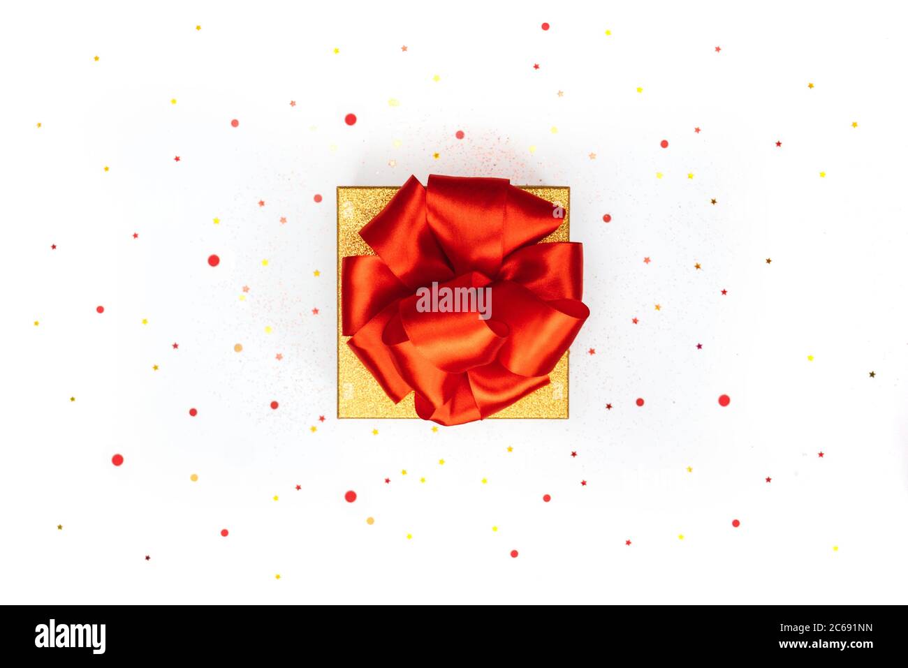 Gold gift box with big red bow on white background with confetti. Top ...