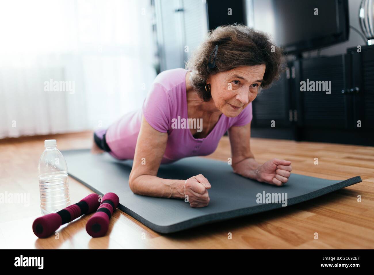 Focused senior woman doing yoga at home. 70 years old woman sitting on  fitness mat with outstretched hands resting on her knees performing yoga in  living room. stock photo - OFFSET