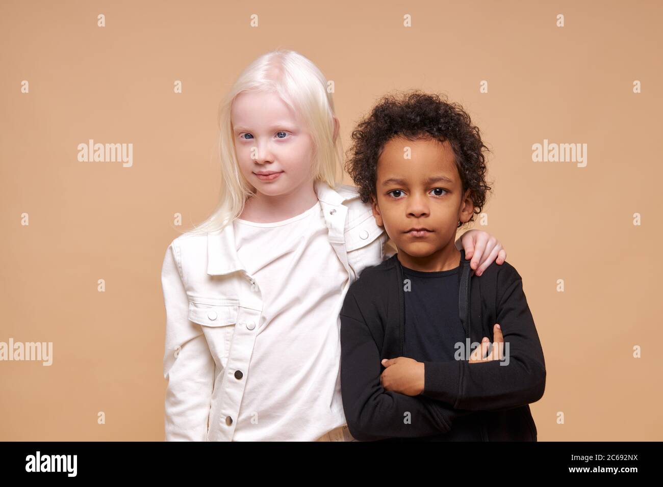 two friendly black afro american and albino children stand together isolated over beige background, diverse positive boy and girl stand hugging. child Stock Photo