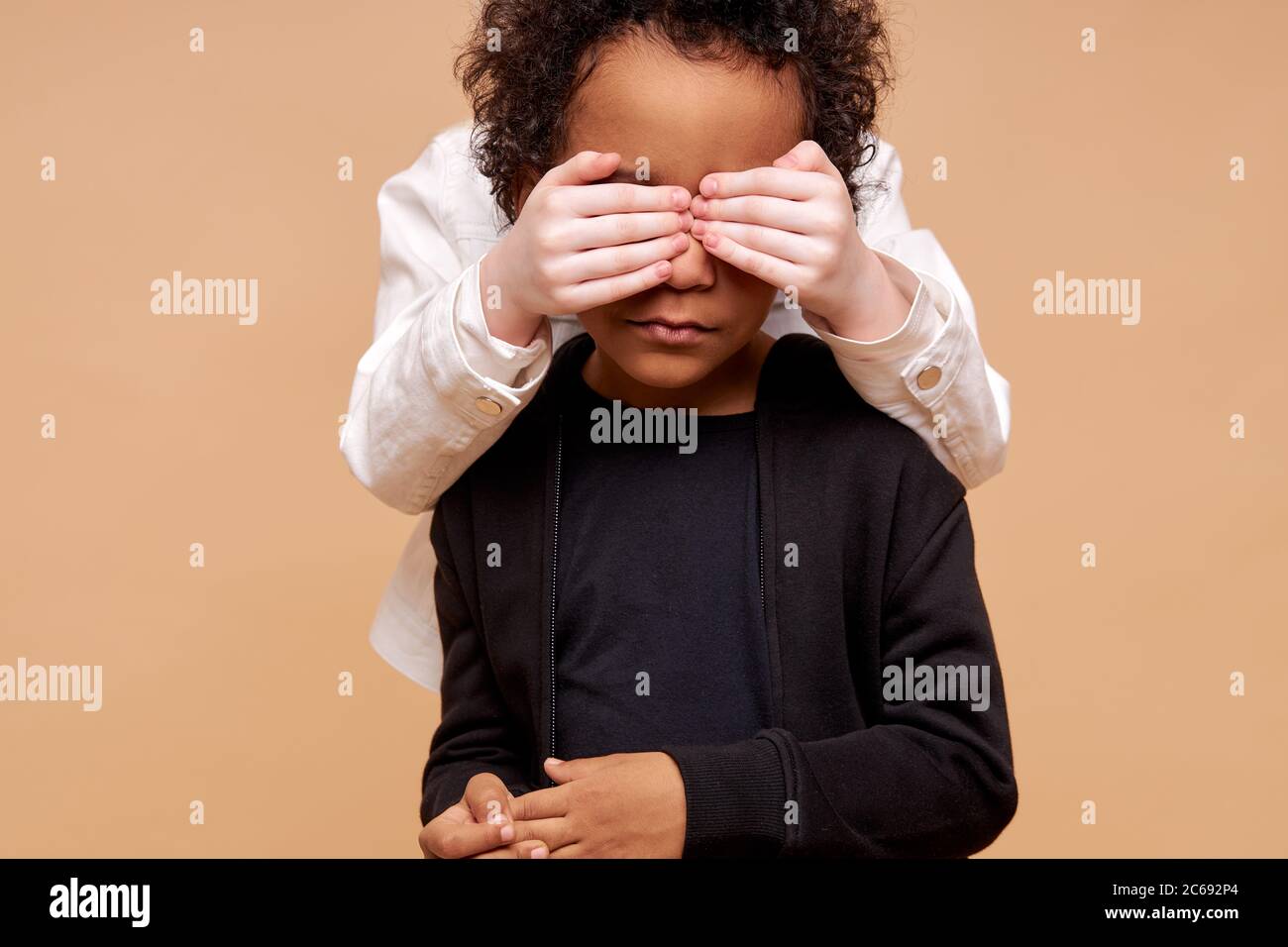unidentifies child girl with pale skin closing african boy's eyes from back, play guess who