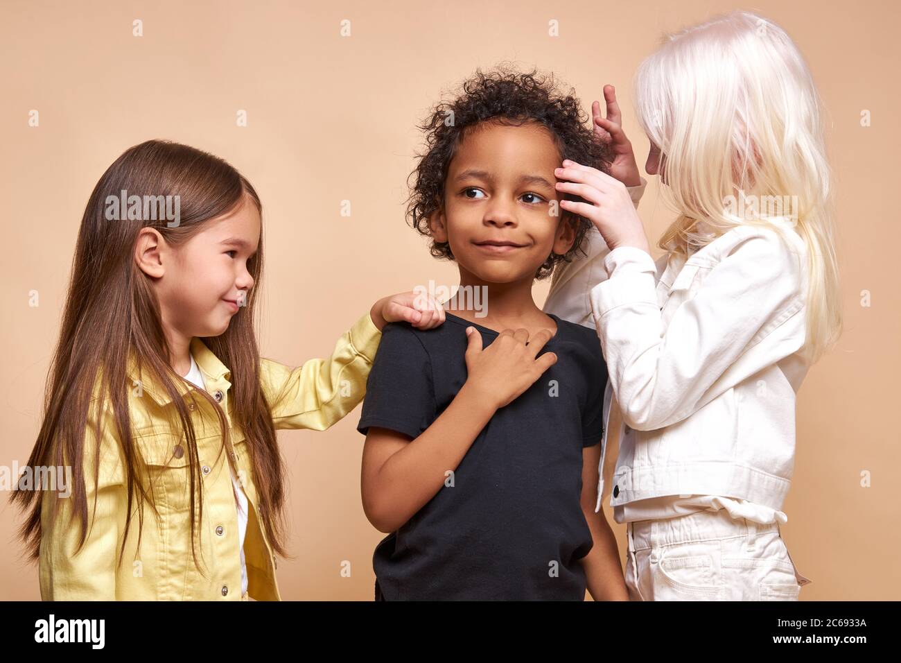 sweet kid girls play with dark-skinned boy, they like him. portrait of diverse children standing together Stock Photo