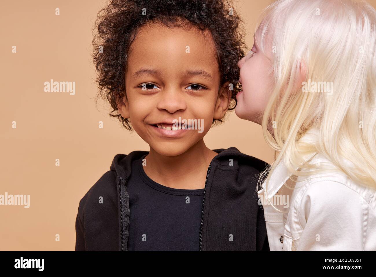 albino girl with pale skin and white hair color tells a secret in the ear  of african boy. cute boy with black skin attentively listen to secret.  isola Stock Photo - Alamy