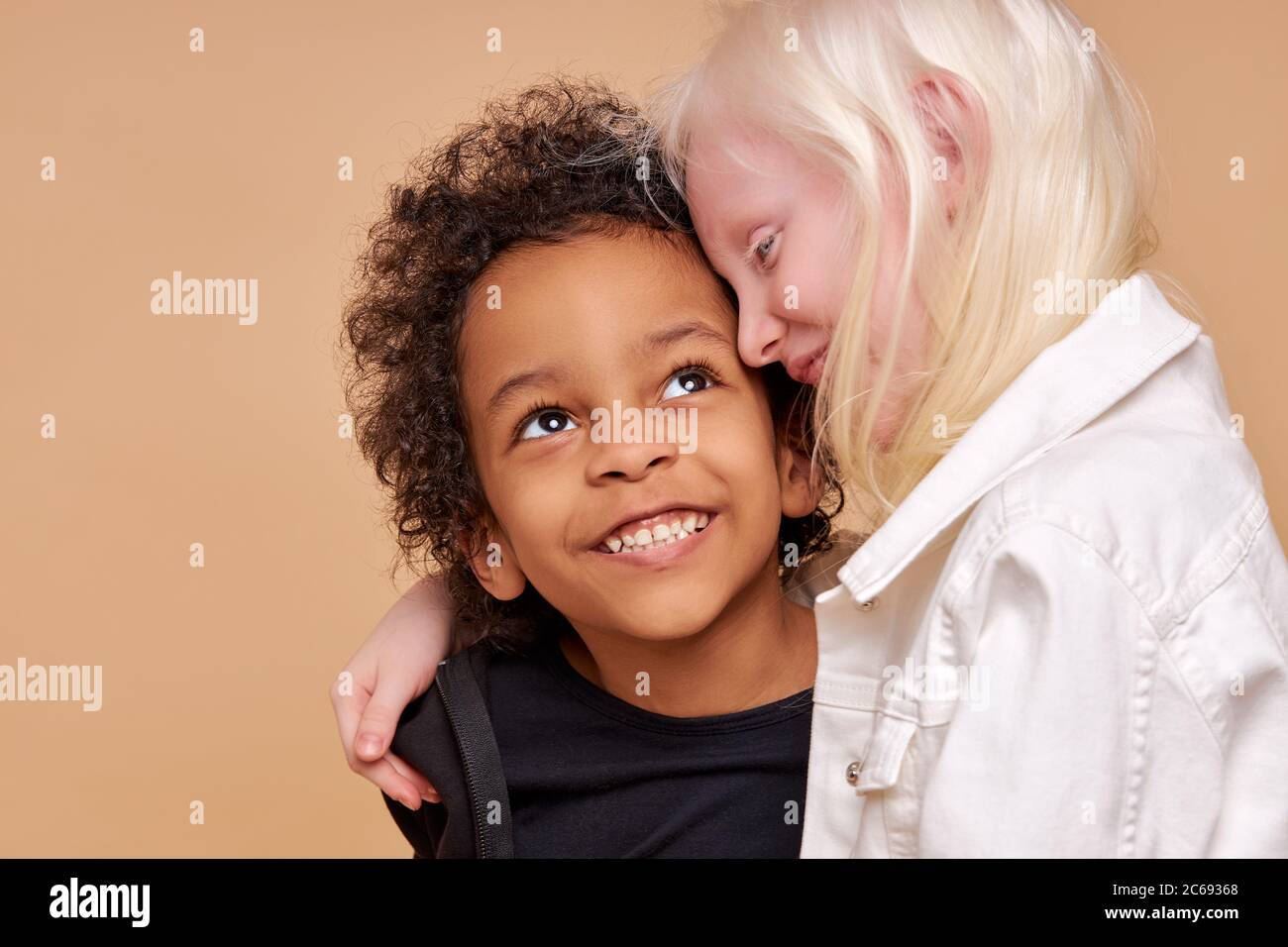 close friendship between two children of different nationalities, beautiful caucasian albino girl and african boy with curly hair, they are hugging Stock Photo