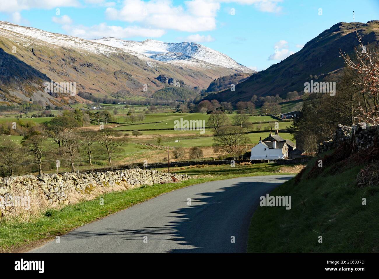 Beautiful sunny day in the Lake District, close to Keswick, with a white farm cottage down in the valley and snow capped peaks in the distance Stock Photo