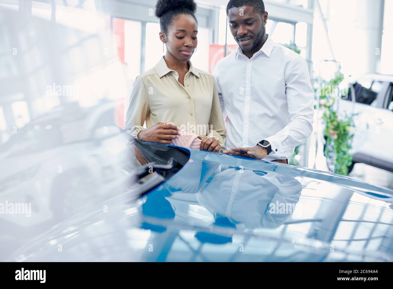 just imagine us on the road. portrait of happy african american couple checking out a car in modern dealership, they choose new car together Stock Photo