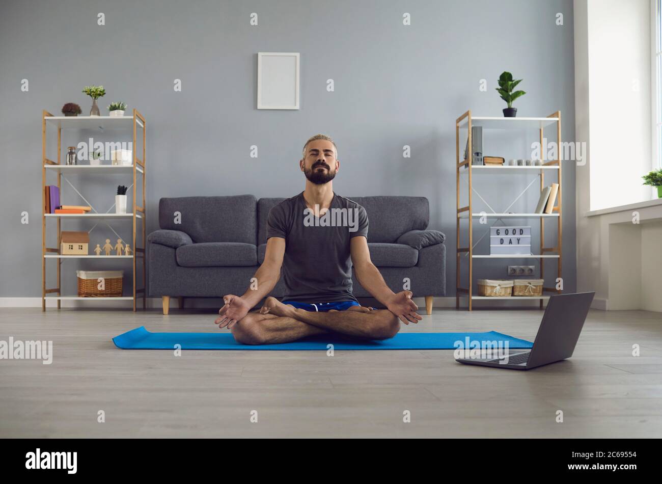 Online yoga class. Peaceful young guy doing morning meditation practice in front of laptop at home. Life balance concept Stock Photo