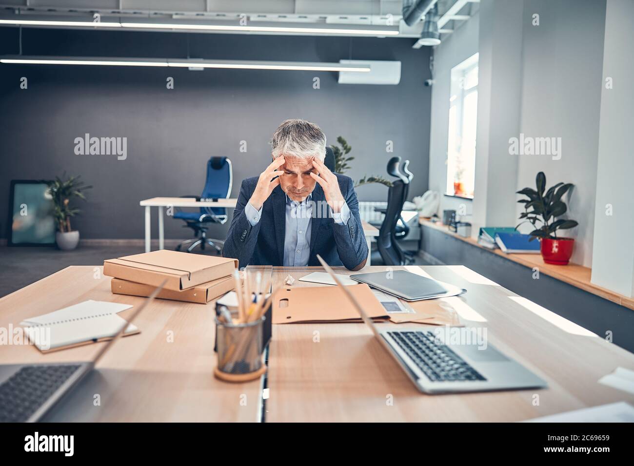 Man at the desk feeling headache and holding two hand Stock Photo