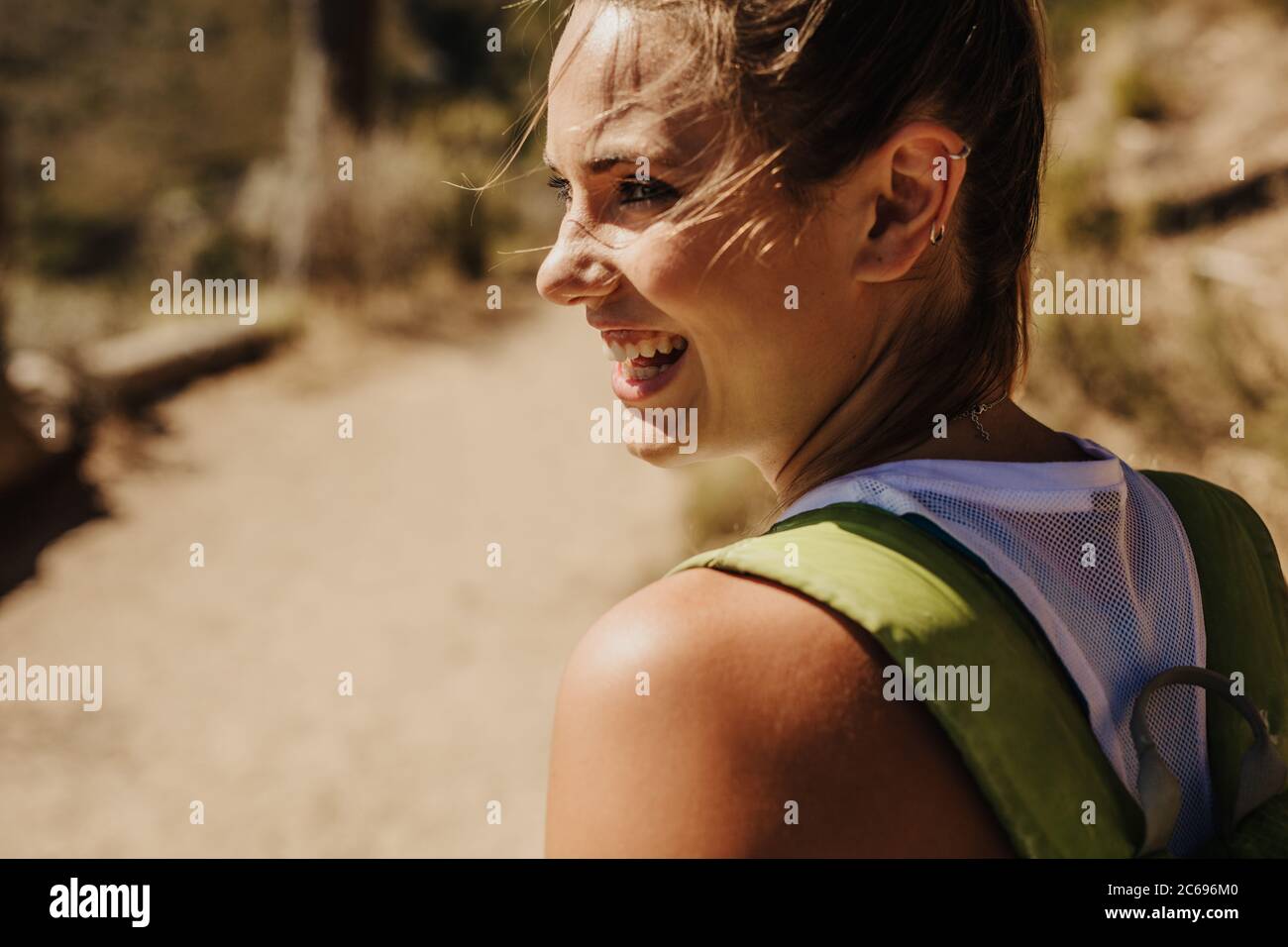 Close-up of a smiling woman hiker on mountain trail. Woman hiking a mountain looking happy. Stock Photo