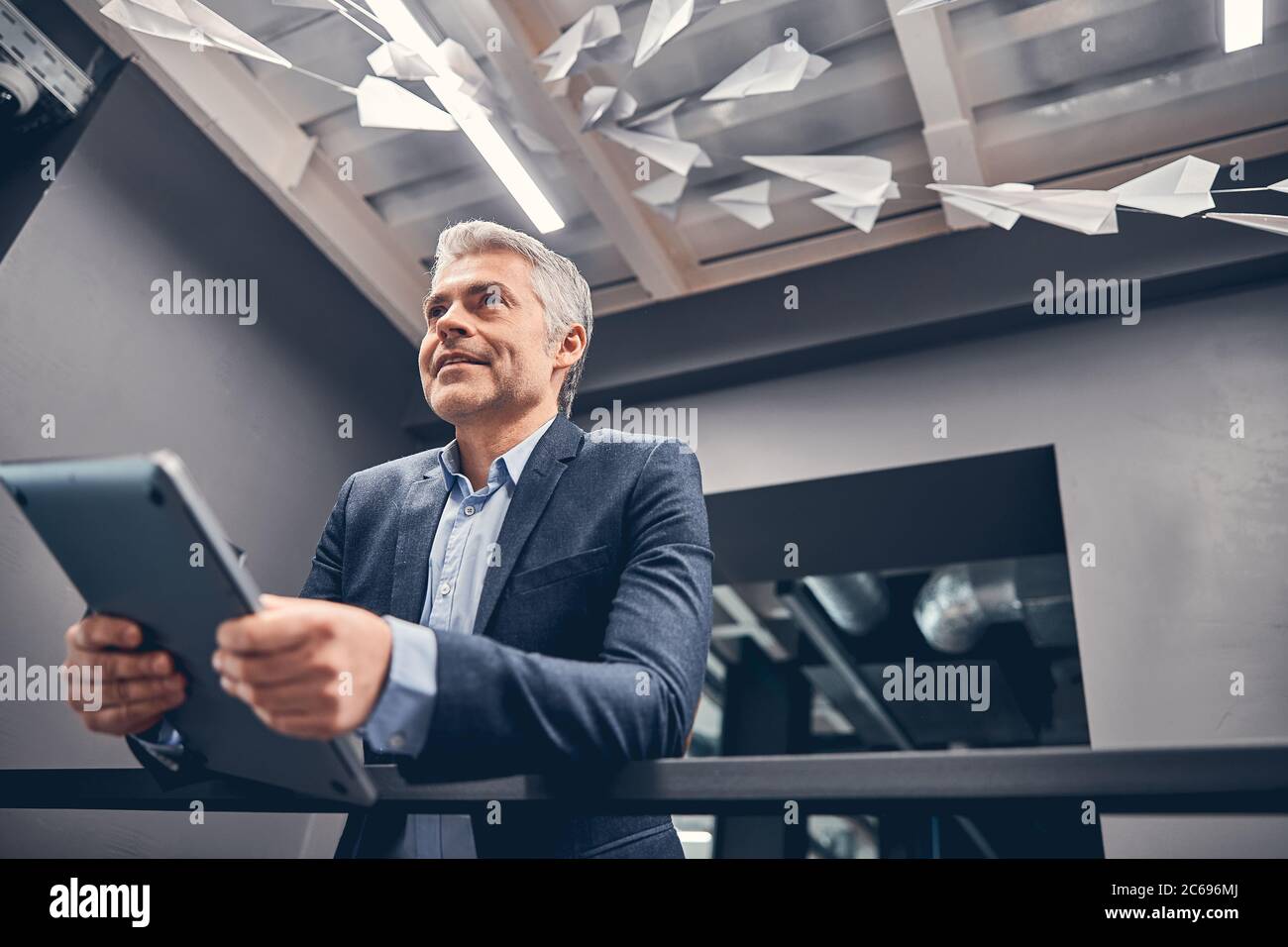 Smiling business man holding laptop while standing at the corridor ...