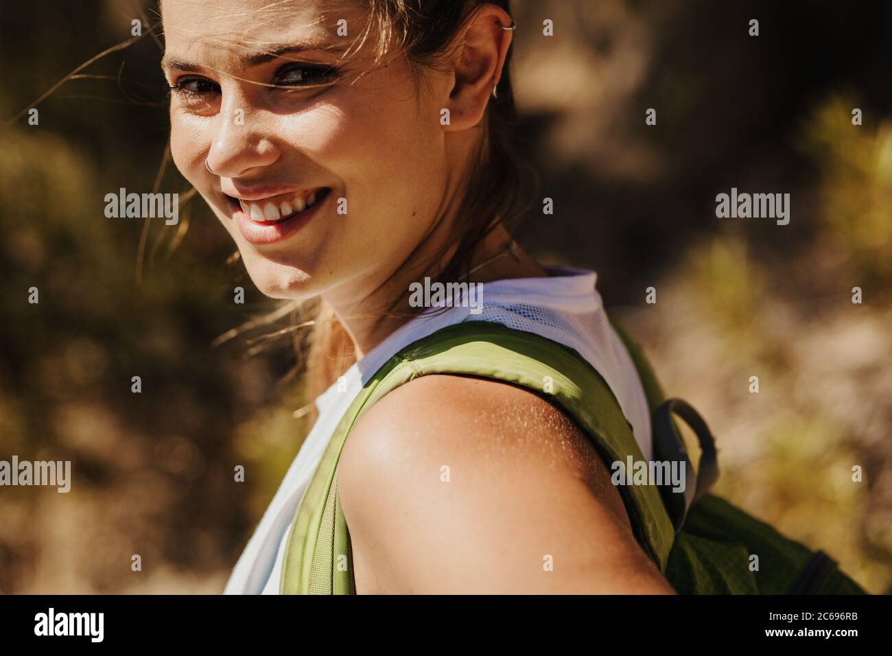 Close-up of a beautiful woman trekker on mountain trail. Female mountaineer climbing a mountain looking at camera and smiling. Stock Photo
