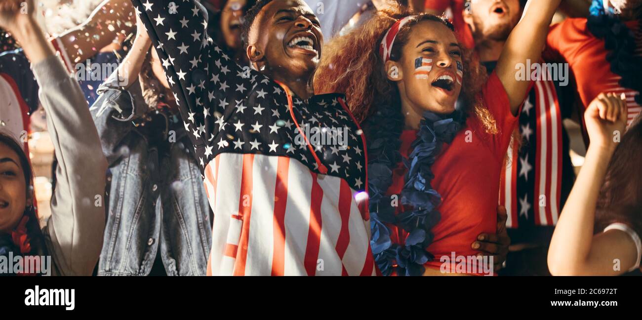 Excited fans in sports crowd, celebrating and cheering on team success. Group of American soccer fans celebrating victory. Stock Photo