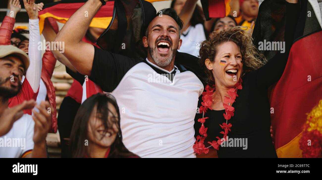 Group of multi-ethnic soccer fans cheering from stadium fan zone. German football supporters celebrating the victory of their national team. Stock Photo