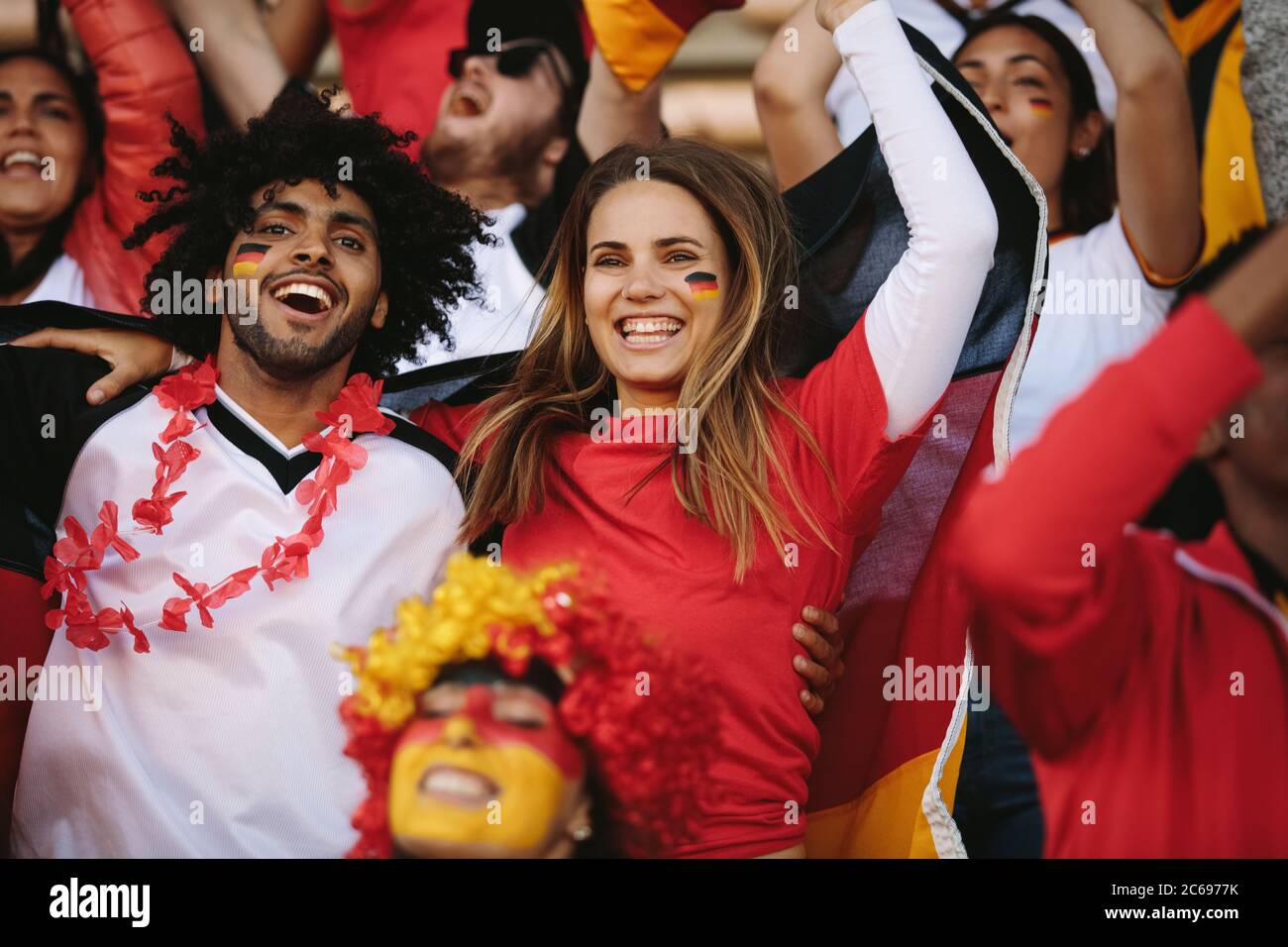 Excited sports fans at live game chanting and cheering for their team. German soccer team supporters watching football match and encouraging their nat Stock Photo