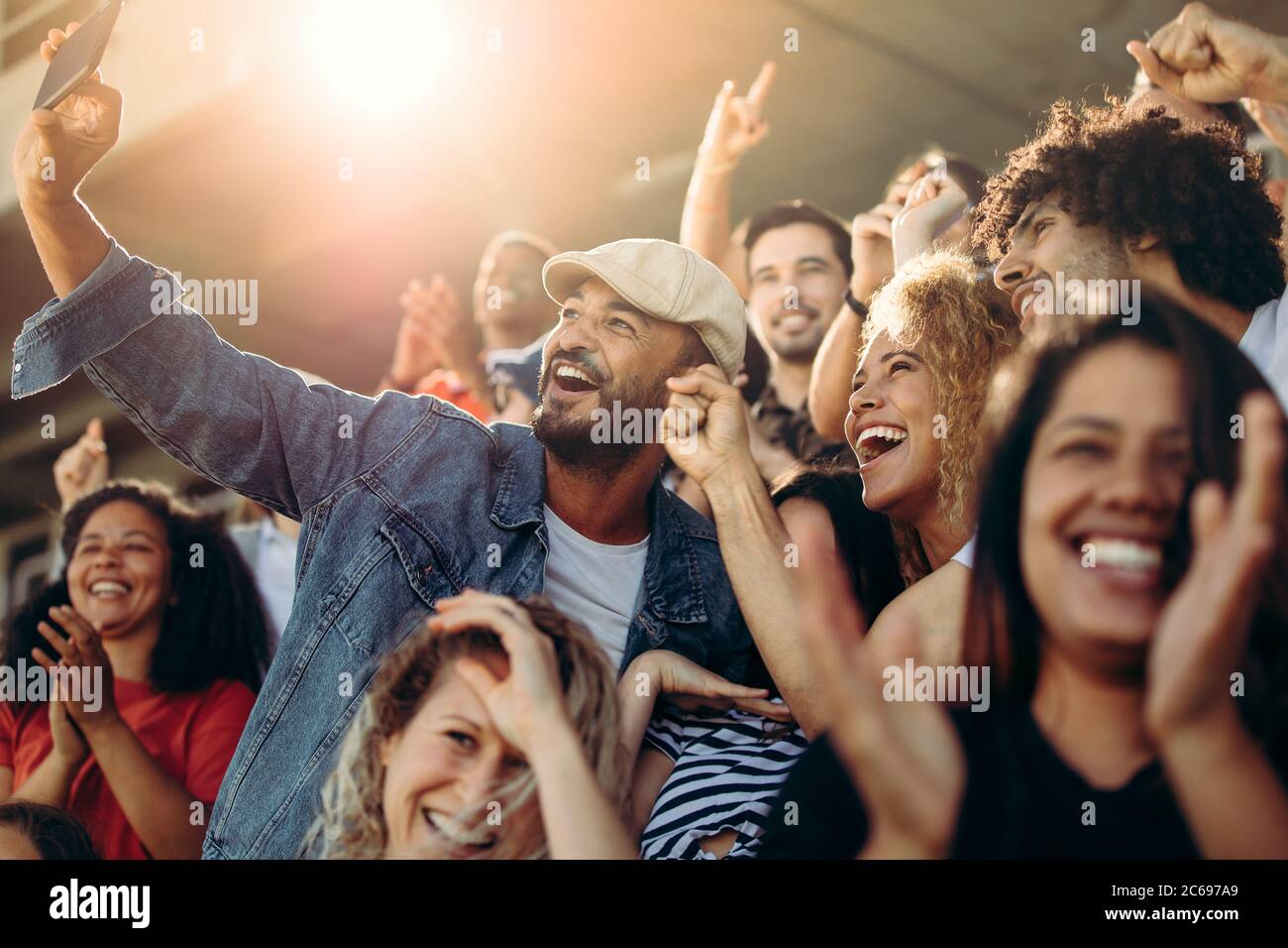 Group of supporters watching football game and making self-portrait with smartphone at stadium. Multi-ethnic people enjoying watching a game at stadiu Stock Photo