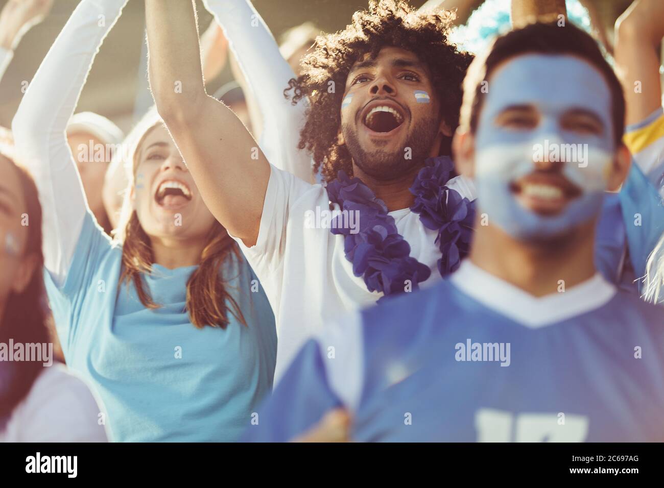 Group of cheering soccer fans from Argentina. Excited sports fans at live football game chanting and cheering for their team. Stock Photo
