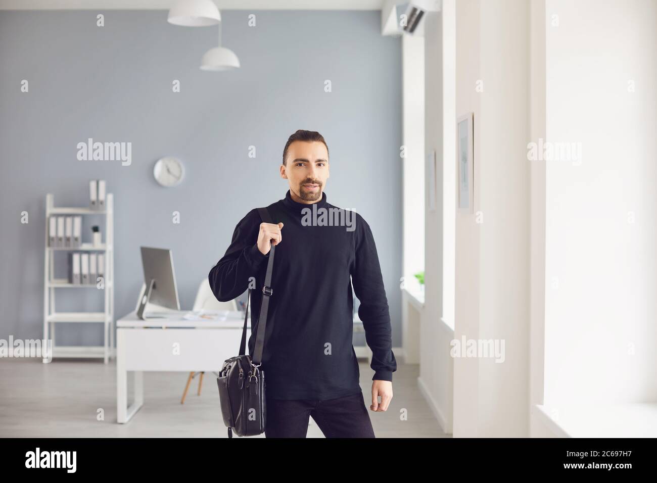Modern man with laptop bag standing in light office Stock Photo