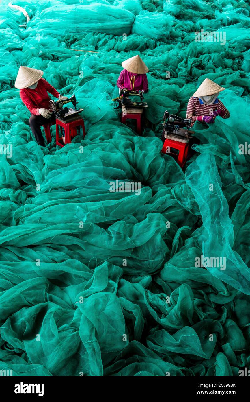 Overhead view of three woman repairing fishing nets, Vietnam Stock Photo