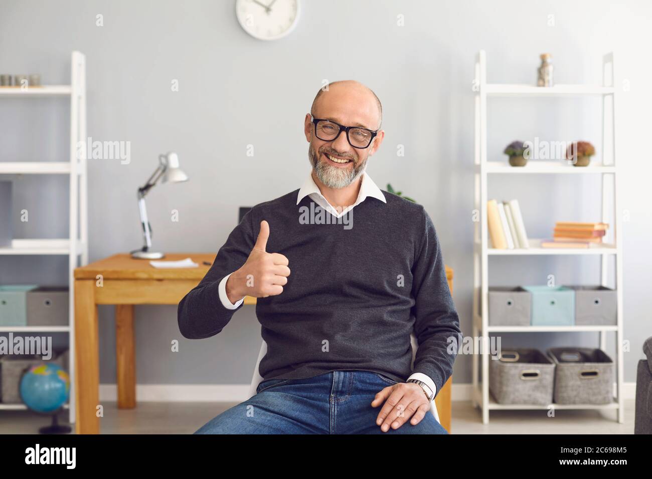 Positive senior man comminucating online, showing thumb up gesture at home. Elderly vlogger broadcasting on webcam Stock Photo