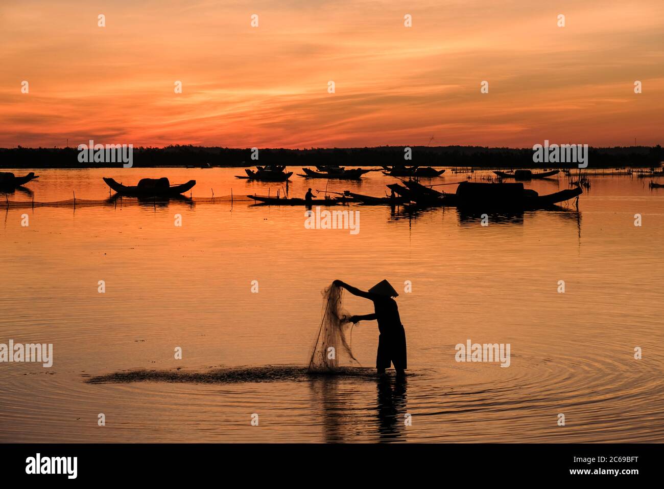 Silhouette of a fisherman standing in river with a fishing net at sunrise, Vietnam Stock Photo