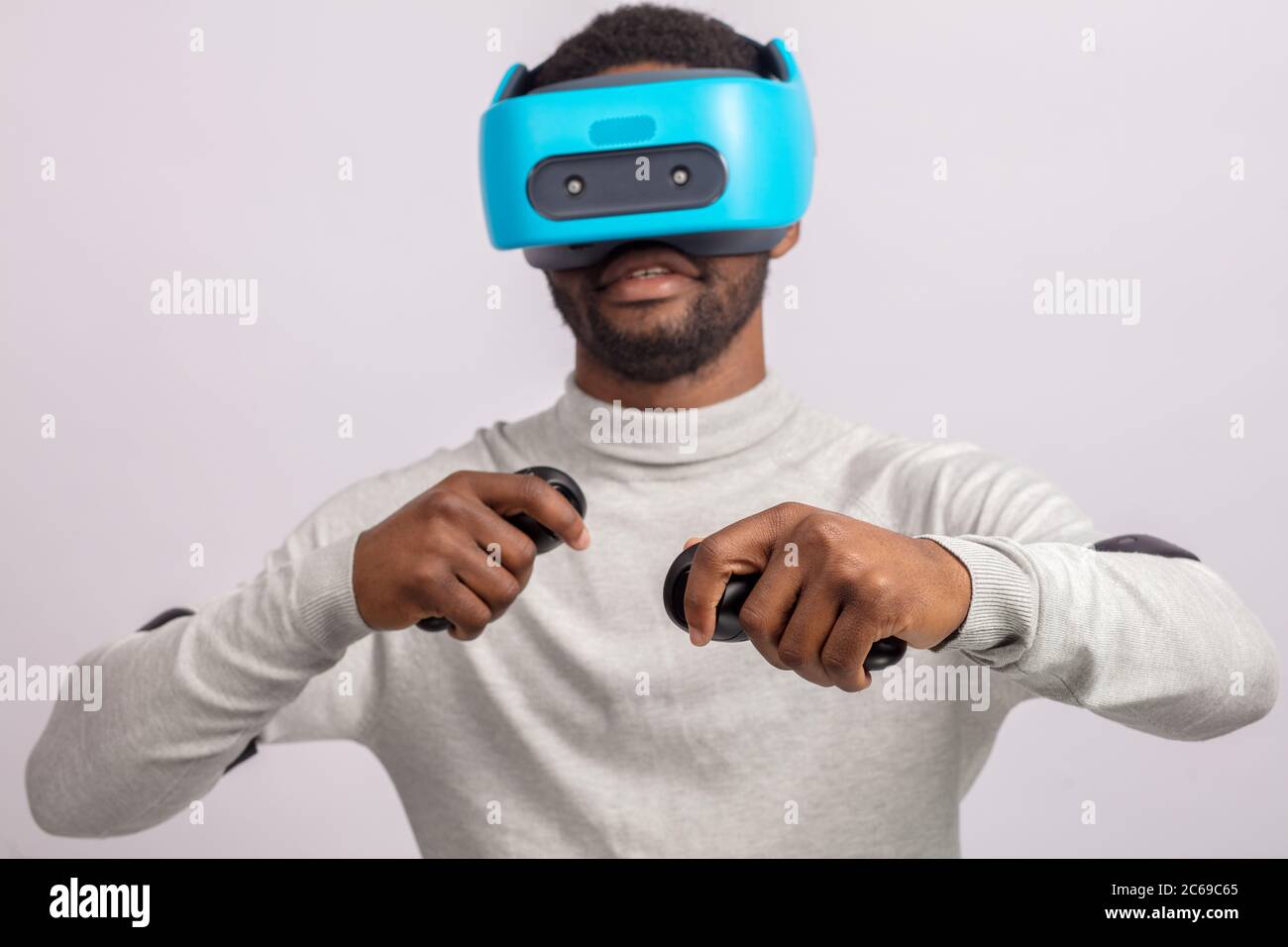 African american guy in casual wear plays racing game in VR headset, holding hands with controllers raised as if he is driving car on high speed in vi Stock Photo