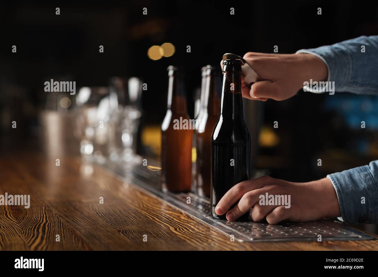 Evening with company in pub. Barman opens beer bottles on wooden bar
