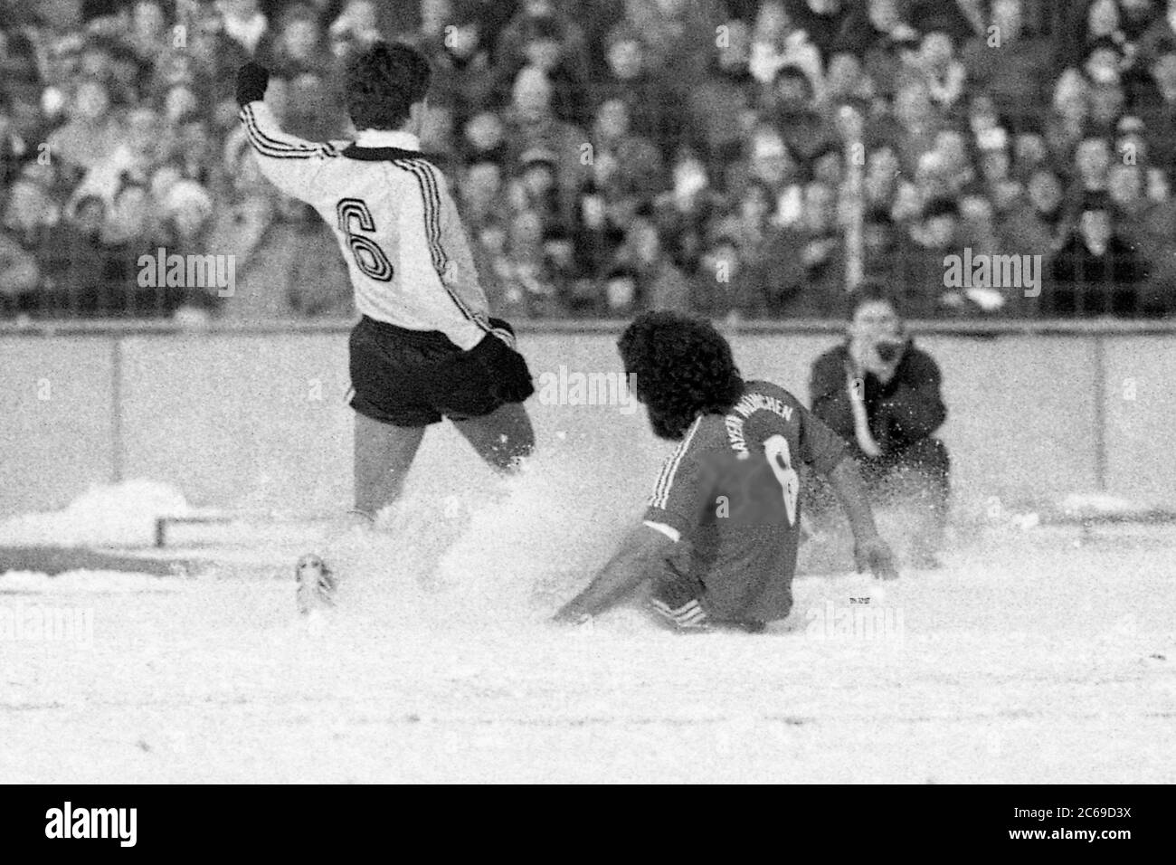 Paul BREITNER (M) grazes on the snow floor versus a Bayreuth player; photographed from behind; Snow, winter, action, game scene; Soccer DFB Pokal SpVgg Bayreuth (BT) - FC Bayern Munich (M) 1-0, on 12.01.1980 in Bayreuth/Germany. | usage worldwide Stock Photo