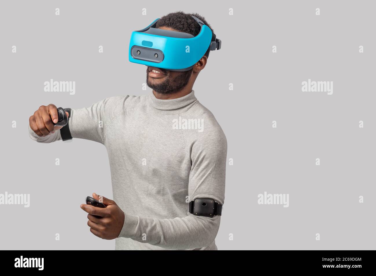 African american guy in casual wear plays racing game in VR headset, holding hands with controllers raised as if he is driving car on high speed in vi Stock Photo