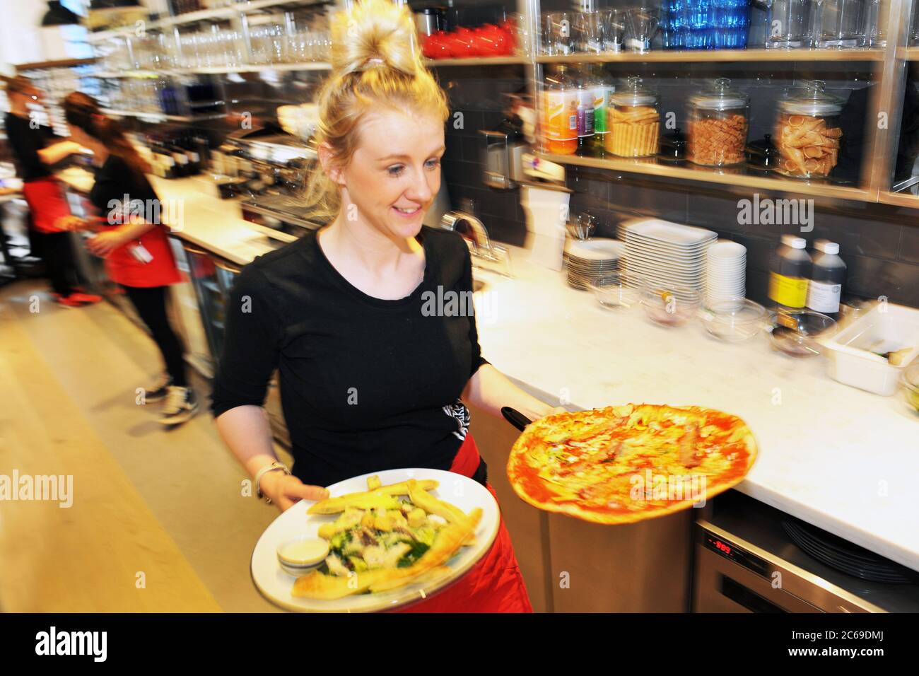 A Young Waitress Carries Pizza In Pizza Express Skipton UK Stock Photo a-young-waitress-carries-pizza-in-pizza-express-skipton-uk-stock-photo