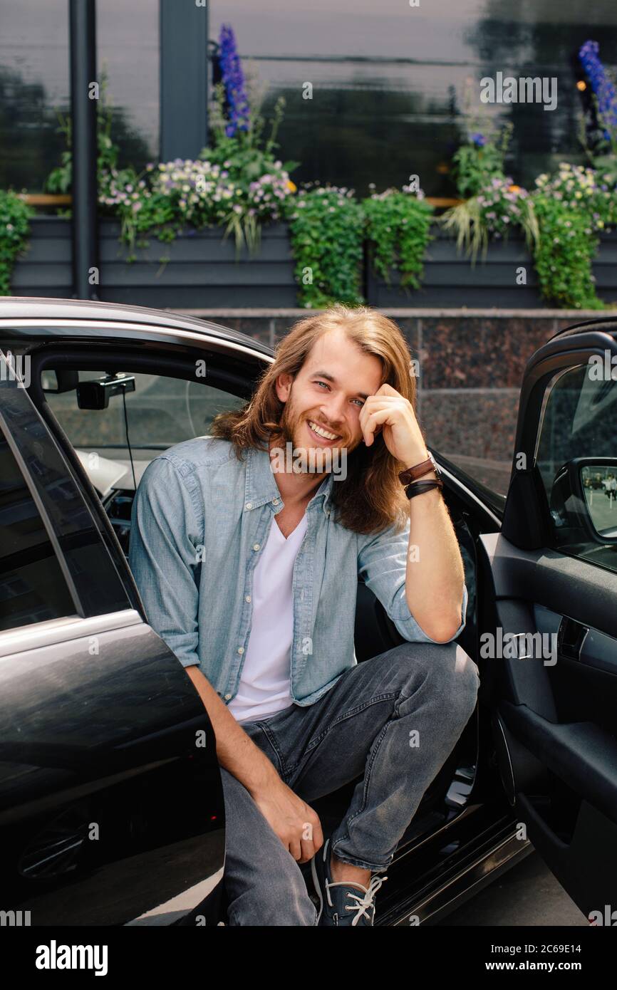 Portrait of a smiling man sitting in a car with the door open Stock Photo