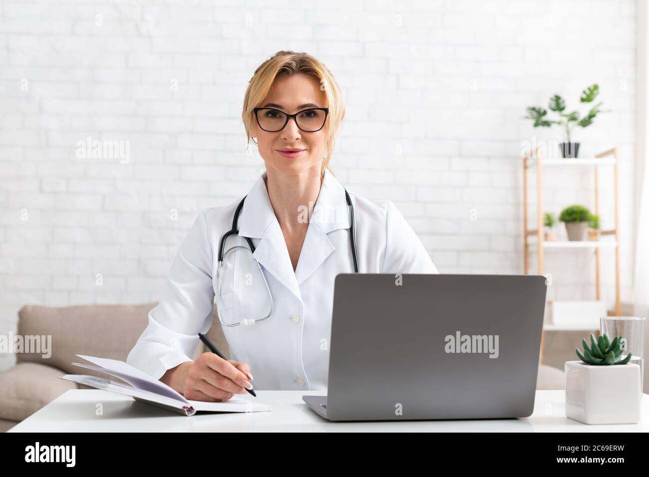 Doctor consultation without leaving home. Woman in white coat writing in notebook Stock Photo