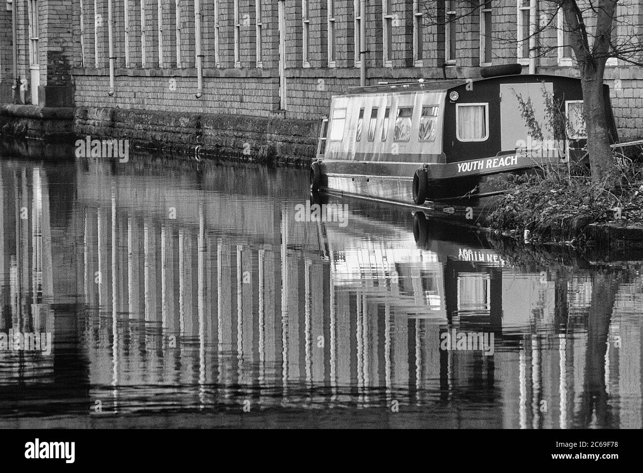 A moored narrowboat and Salts Mill reflected in the Leeds and Liverpool Canal at Saltaire, West Yorkshire, England, UK Stock Photo