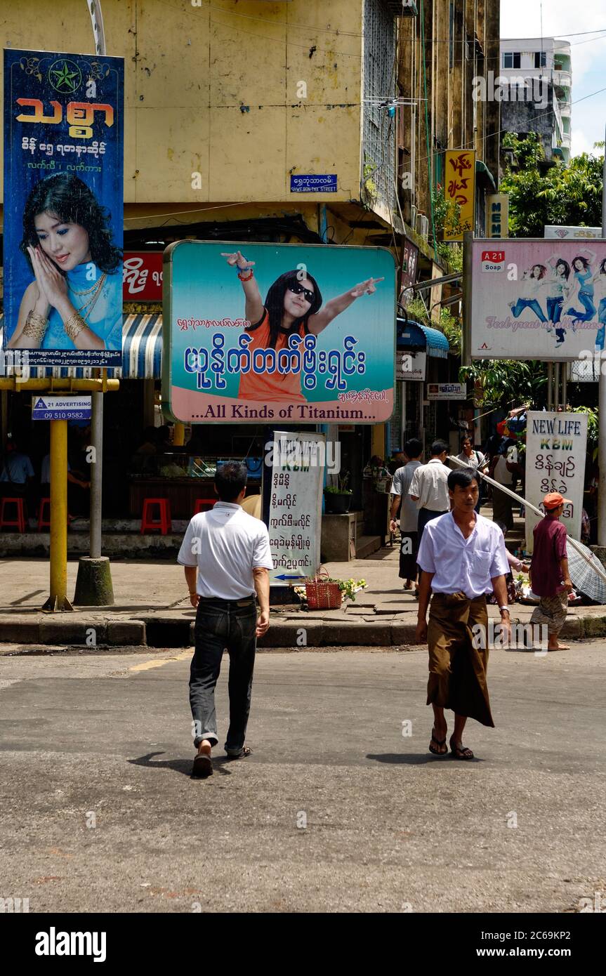 Two men crossing the road in Yangon, one in traditional sarong, the other in modern jeans. Myanmar. Stock Photo