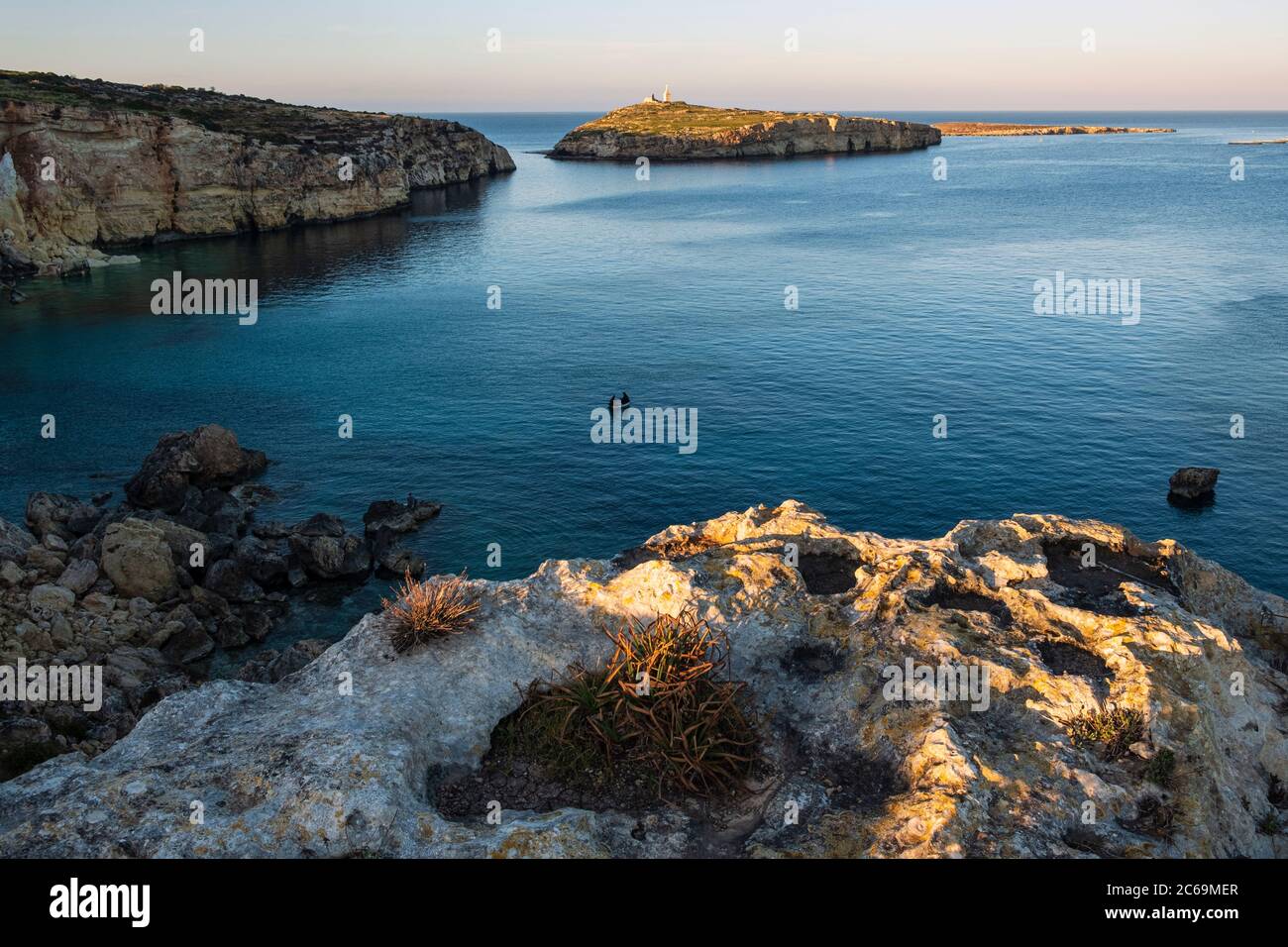 Evening view towards Selmunett or Saint Paul's Islands and two men fishing from a boat, Malta Stock Photo