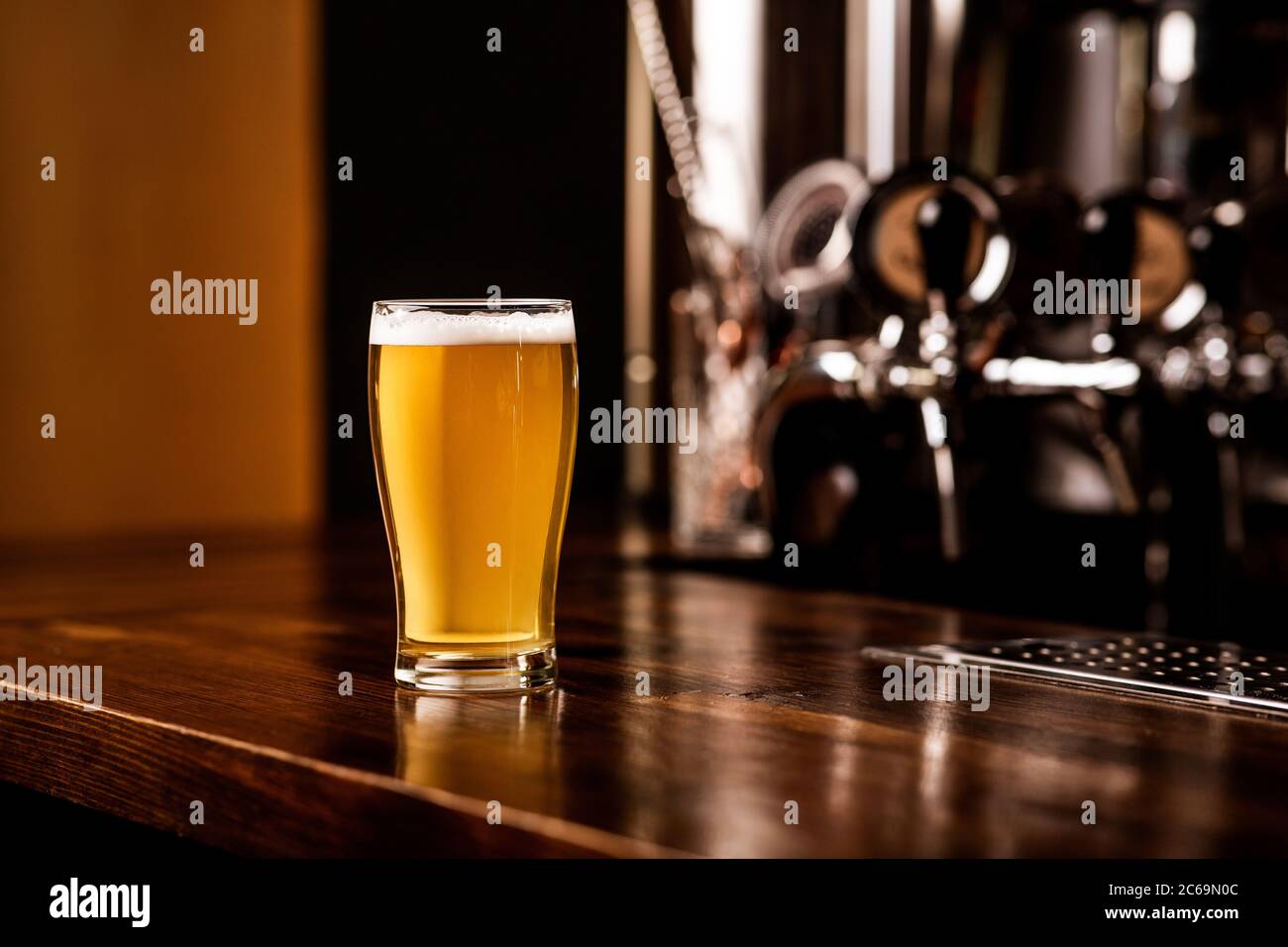 Light beer in glass. Ale with foam on brown wooden counter, metal taps near Stock Photo