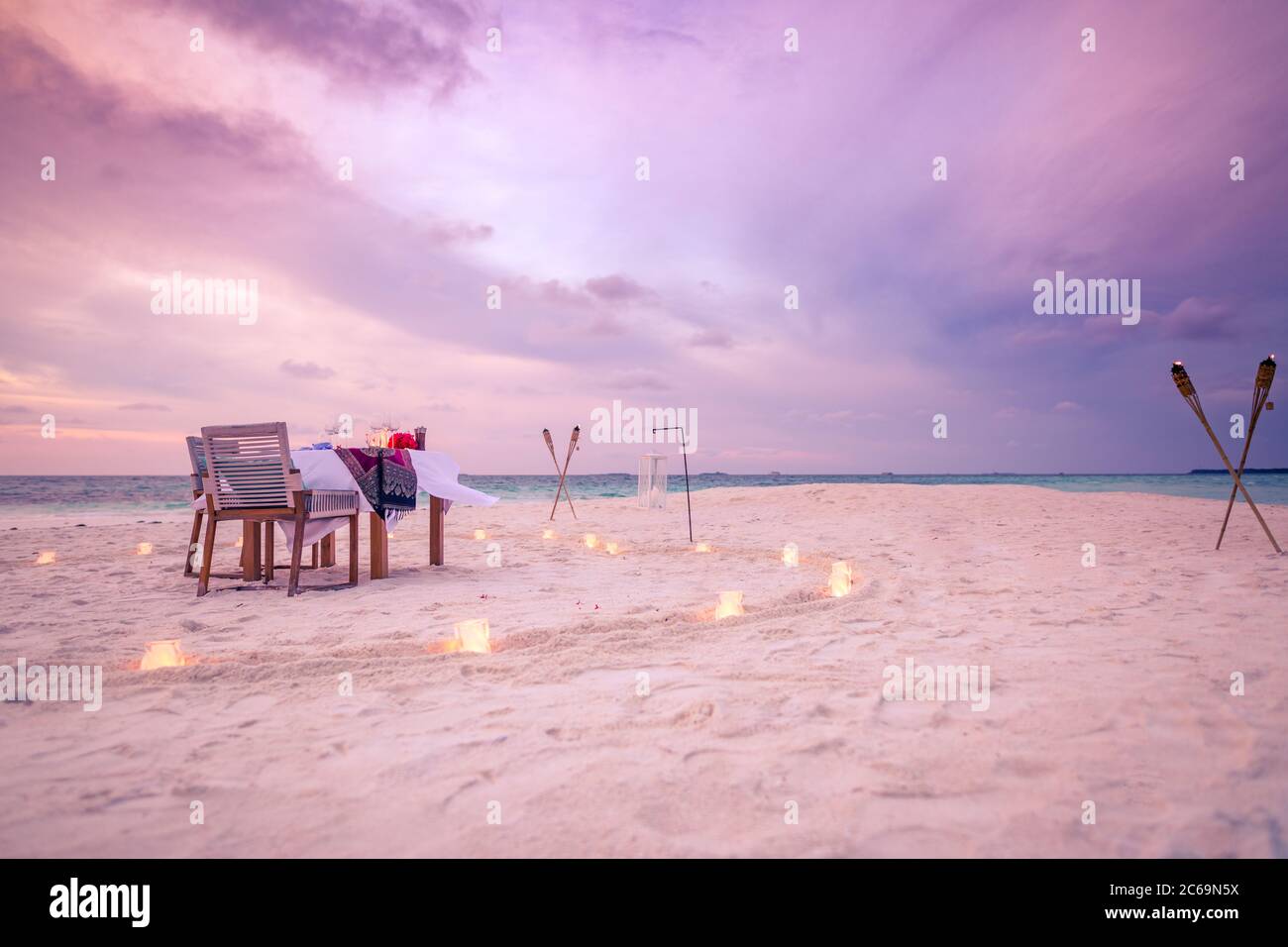 Romantic beach dinner with sunset with candles and in heart shape. Couple destination dining in luxury honeymoon vacation and travel scenery Stock Photo