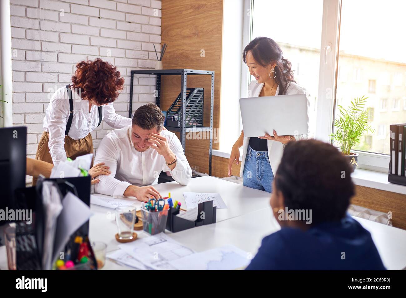 smiling male sit on table while asian woman with laptop speaking. Stock Photo