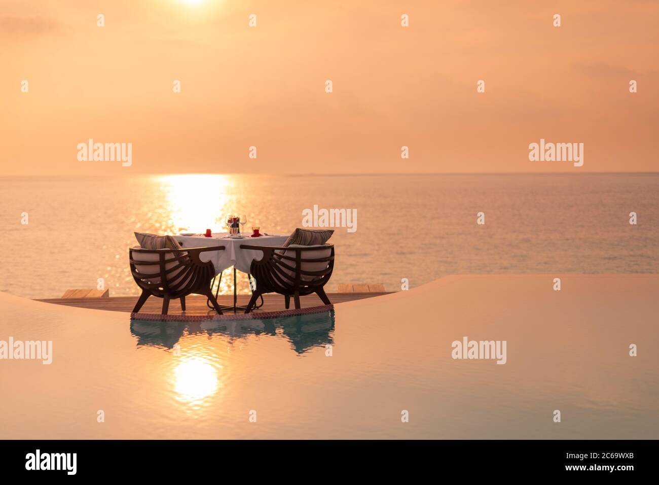 Dining table in the sunset moment. Romantic dinner on the beach, amazing sunset sea reflection. Romantic mood, couple travel vacation Stock Photo