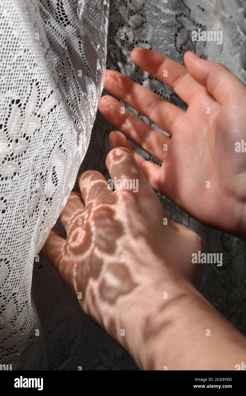 Young Woman With Shadows From A Lace Curtain On Her Hands Stock Photo