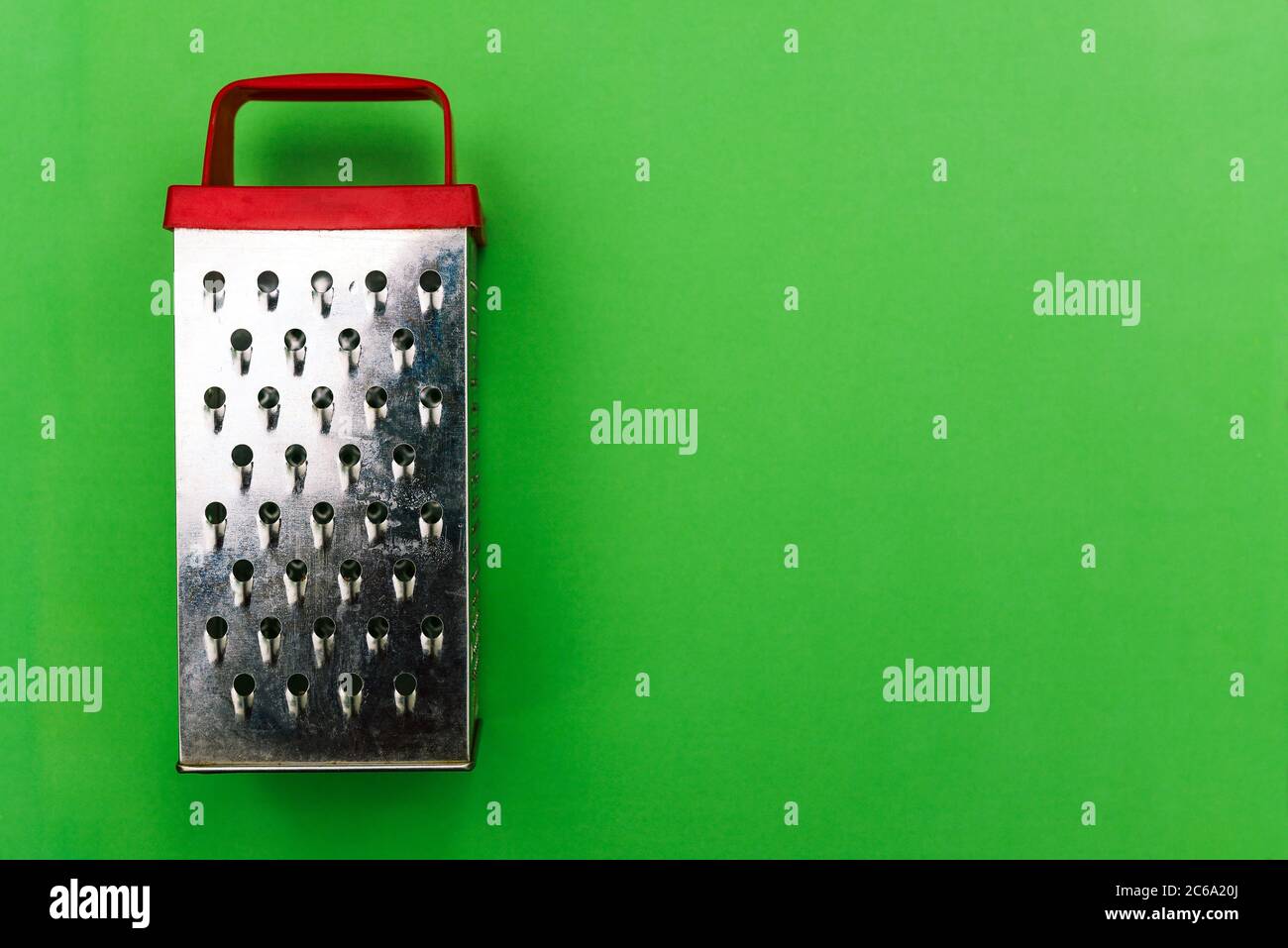 Metal grater with a red handle on a green background. Grater for vegetables and products. Kitchen grater close-up with a copy of the space. A top view Stock Photo