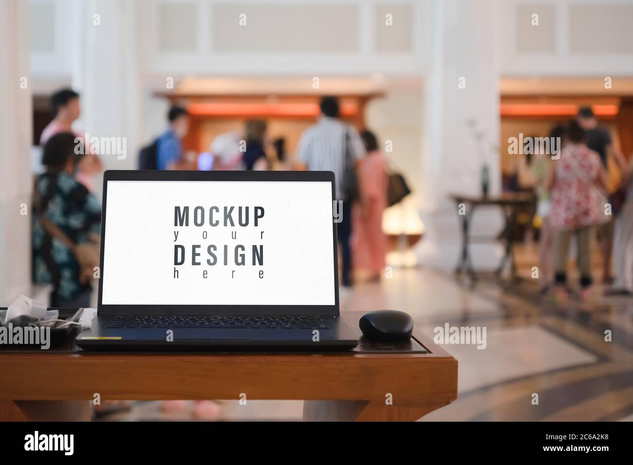 Mockup blank white screen laptop with blurred people waiting for registration in hotel hall Stock Photo