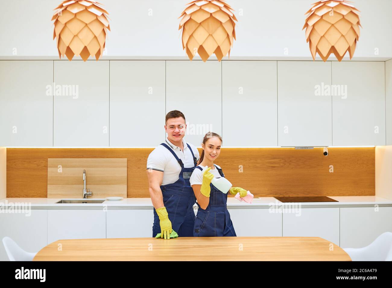 Successful team work of two janitors after work, posing in working blue uniforms, look at camera. White kitchen background Stock Photo