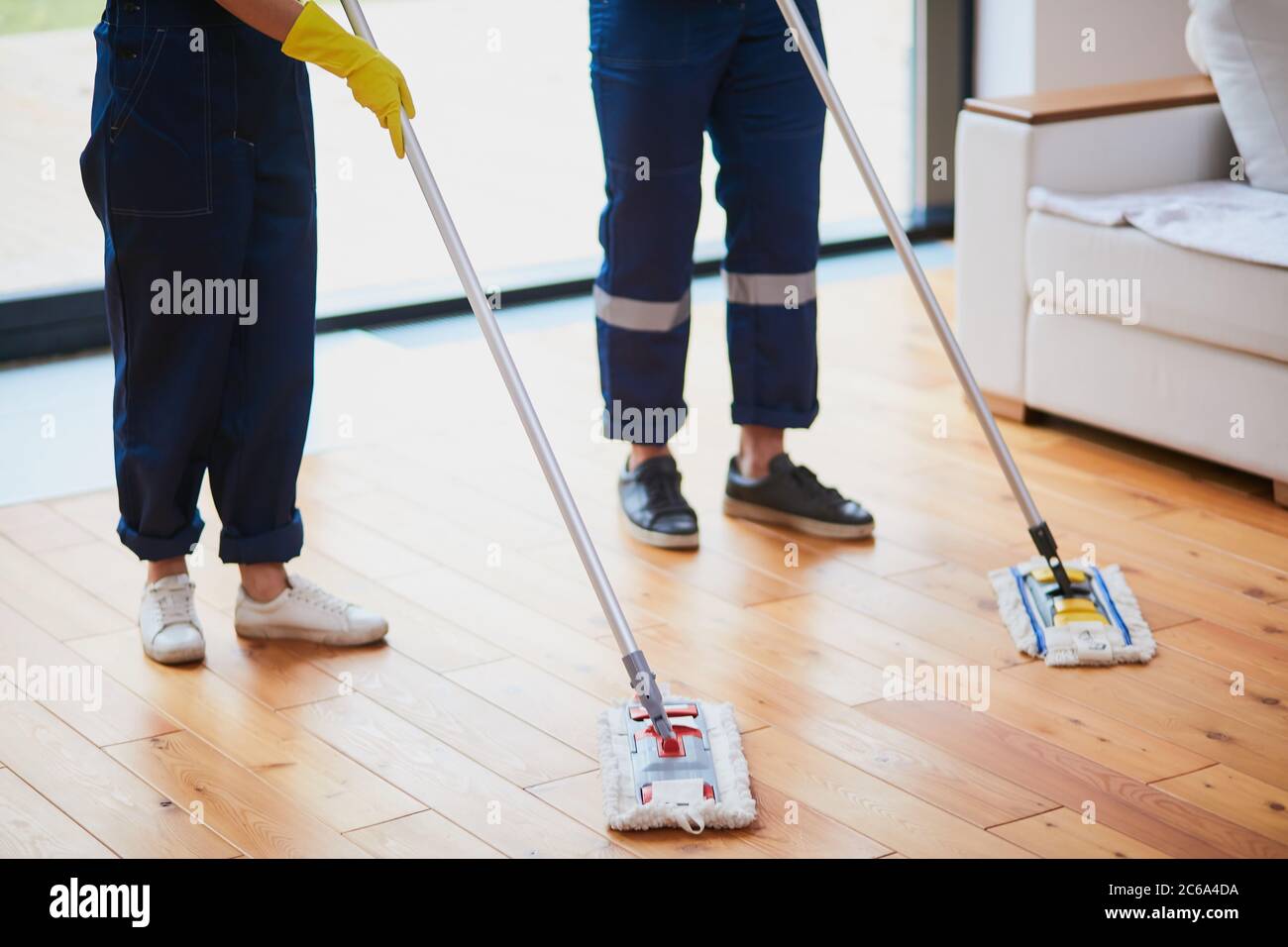 Closeup of janitors legs washing wooden floor with mops. Cleaning