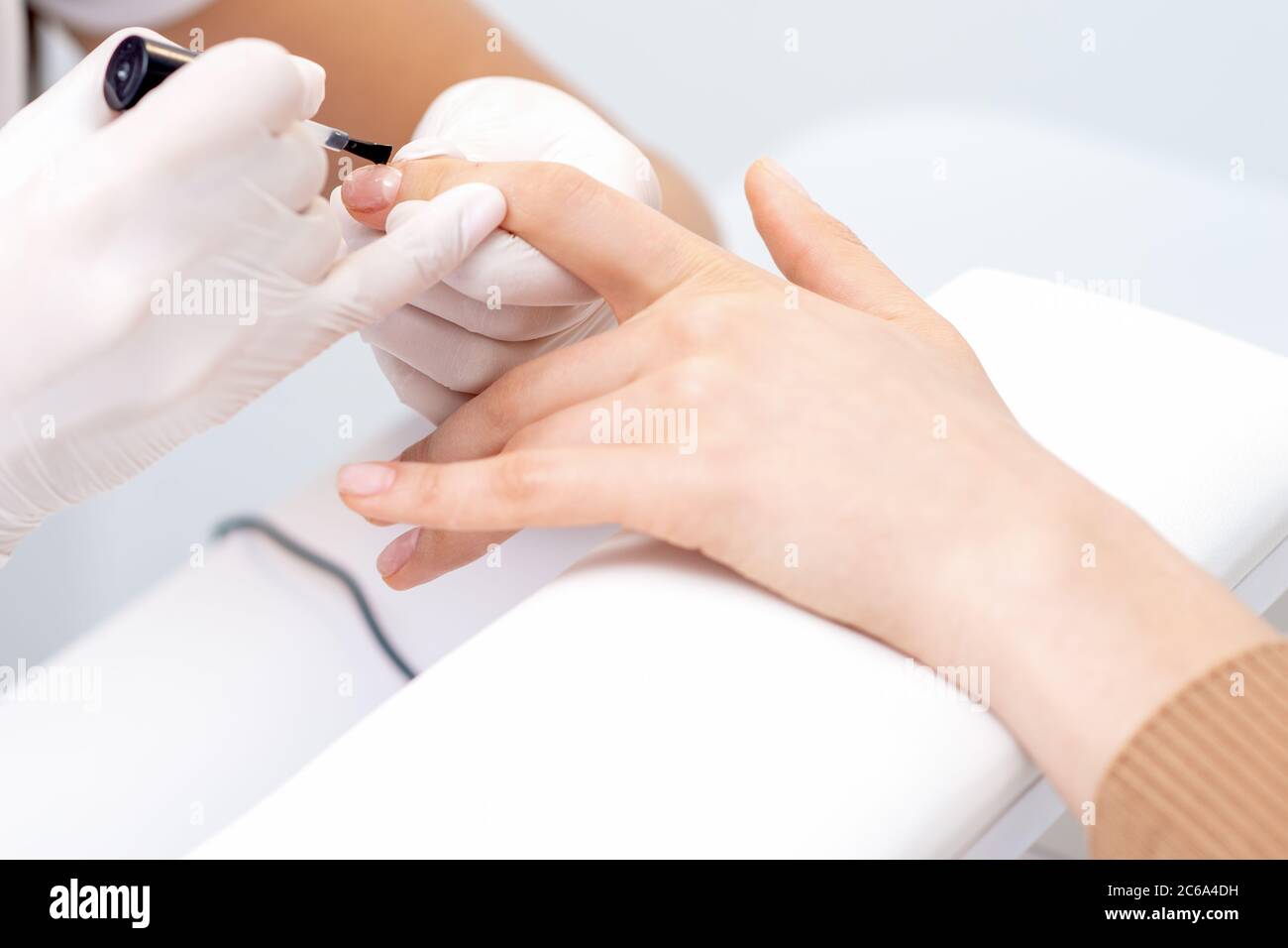 Human hands in protective gloves covering clear varnish on female nails Stock Photo