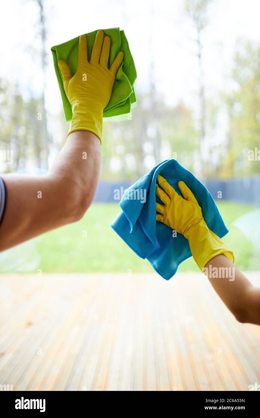 Closeup of cleaners holding rags, wearing yellow rubber gloves. Cleaning glass of window Stock